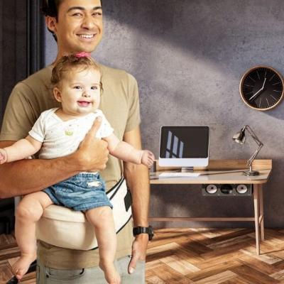 bébé-tenu-dans-les-bras-de-son-papa-sur-son-porte-bébé-beige-dans-son-bureau-regardant-le-monde-en-étant-souriant
