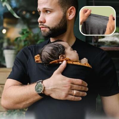 bébé-installé-dans-son-porte-bébé-physiologique-T-shirt-noir-dans-les-bras-de-son-papa-à-coté-d-un-jardin