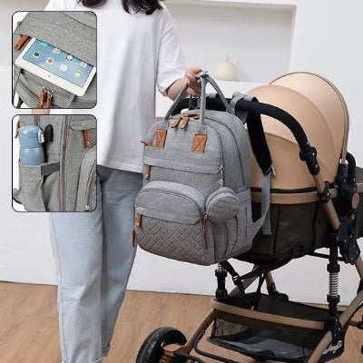 Maman-accrochant-son-sac-à-dos-à-langer-gris-à-sa-poussette-contenant-une-tablette-et-une-bouteille-isotherme-placées-dans-leur-compartiment-spécifique