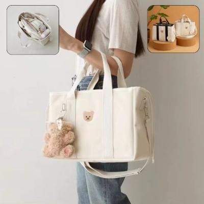 Jeune-maman-au-cheveux-longs-dans-son-salon-porte-au-bras-son-sac-langer-beige-au-design-élégant-et-contemporain-de-grande-taille-sur-lequel-est-cousu-une-tête de-nounours-marron-et-est-accroché-un-porte-clé-nounours marron-clair-à-pieds-roses
