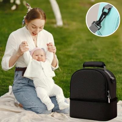 maman-joue-avec-son-bébé-vêtu-d-un-ensemble-blanc-et-d-un-bonnet-rose-à-côté-de-son-sac-à-langer-noir-à-fermeture-éclaire-et-poignée-confortable-dans-un-jardin-public-une-après-midi