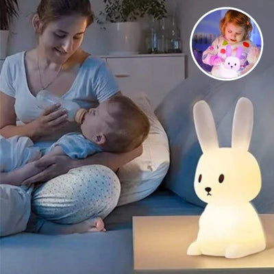 Maman-assise-sur-son-canapé-donnant-le-biberon-à-son-bébé-à-côté-duquel-est-posé-sur-une-table-sa-veilleuse-bébé-en-silicone-doux-au-toucher-