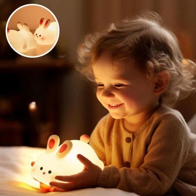 Bébé-manipulant-sa-veilleuse-bébé-en-forme-de-lapin-en-silicone-doux-sur-son-lit-lui-donnant-le-sourire