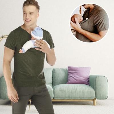 bébé-porte-un-bonnet-tricoté-bleu-et-dort-dans-son-porte-bébé-physiologique-T-shirt-vert-dans-les-bras-de-son-papa-dans-le-salon-à-côté-du-canapé
