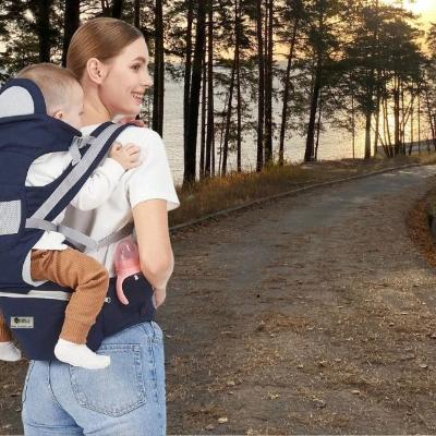 bébé-est-dans-son-porte-bébé-randonnée-bleu-marine-dans-le-dos-de-sa-maman-sur-un-chemin-menant-à-un-lac-en-fin-d-après-midi-un-soir-d-été