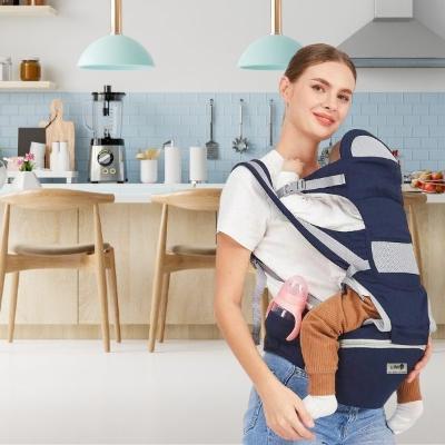 bébé-est-dans-son-porte-bébé-randonnée-bleu-dans-lequel-se-trouve-un-biberon-rose-installé-dans-la-poche-spécialement-prévu-à-cet-effet-face-à-sa-maman-qui-est-dans-sa-cuisine