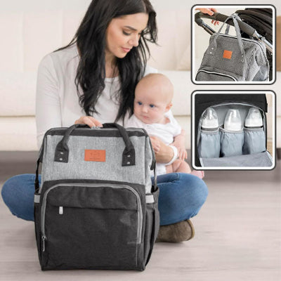 Bébé-assis-sur-les-genoux-de-sa-maman-dans-son-salon-à-côté-de-son-sac-à-dos-à-langer-gris-et-noir-à-l-intérieur-duquel-se-trouvent-des-biberons-de-lait