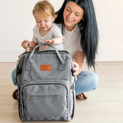 Bébé-assis-sur-les-genoux-de-sa-maman-attrapant-les-poignées-souples-renforcées-de-son-sac-à-dos-à-langer-gris-clair-dans-son-salon