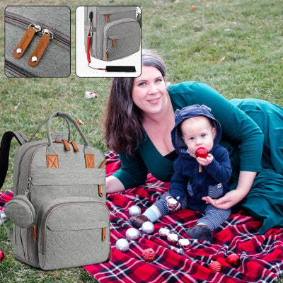Maman-allongé-sur-une-couverture-sur-laquelle-se-trouve-son-sac-à-dos-à-langer-gris-à-port-usb-avec-son-bébé-en-picque-nique-dans-un-parc