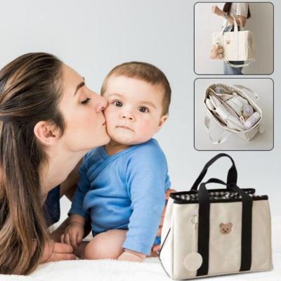 Maman-embrassant-son-bébé-sur-son-lit-à-côté-duquel-se-trouve-son-sac-à-langer-beige-et-noir-au-design-élégant-et-contemporain-dans-lequel-sont-rangés-biberons-couches-matelas-à-langer-lingettes-mouchoirs