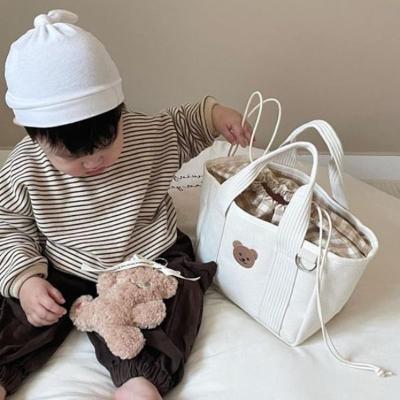 Bébé assis lit chambre à côté sac à langer toile beige design nounours