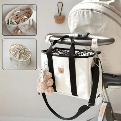 Sac-à-langer-de-grande-taille-au-design-élégant-beige-et-noir-accroché-à-une-poussette-et-fermé-avec-du-tissu-vichy-de-couleur-noir-et-blanc
