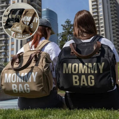 2 jeunes-femmes-assise-dans-un-coin-de-verdure-au-milieu-des-gratte-ciel-portant-sur-leur-dos-chacune-le-même-sac-à-langer-spacieux-marron-et-noir-design-et-esthétique-faisant-office-de-sac-à-dos-de-tous-les-jours