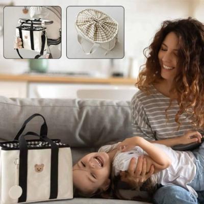 Jeune-maman-jouant-avec-son-bébé-dans-son-salon-sur-son-canapé-sur-lequel-est-posé-son-sac-à-langer-au-design-élégant-et-contemporain-de-grande-taille-noir-et-beige-à-tête-de-nounours-marron