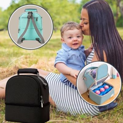 bébé-est-assis-sur-les-jambes-de-sa-maman-côté-de-son-sac-à-langer-noir-à-poignée-dans-un-pré-entouré-d'arbres
