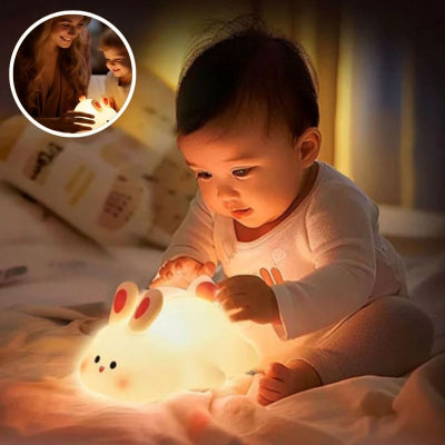 Bébé-assis-sur-un-grand-lit-admirant-la-lumière-de-sa-veilleuse-bébé-en-forme-de-lapin-accroupi-lui-illuminant-son-visage-de-bambin
