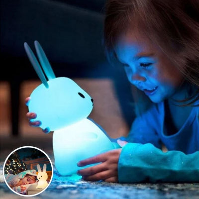 Jeune-enfant-allongé-sur-son-tapis-de-chambre-tenant-entre-ses-mains-sa-veilleuse-bébé-en-forme-de-lapin-de-couleur-bleue-et-étant-admirative