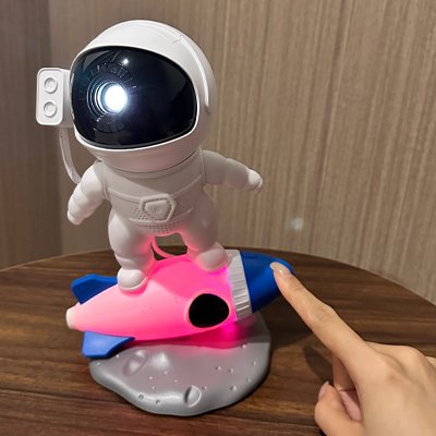 Veilleuse bébé projection plafond design astronaute sur fusée colorée posée sur table