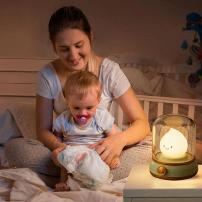 Maman-jouant-avec-son-bébé-sur-son-lit-dont-le-visage-est-éclairé-par-sa-veilleuse-bébé-verte-style-rétro-à-lumière-douce-batterie-rechargeable-de-120-heures
